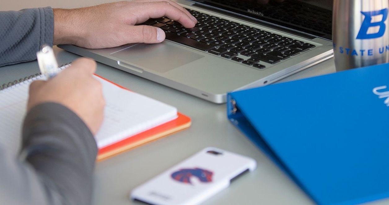Student works at a desk, surrounded by Boise State office supplies and a laptop.