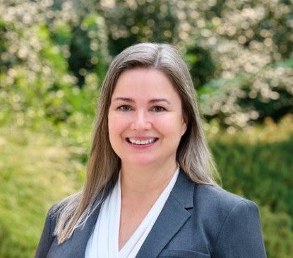 Photo of woman, prelaw advisor in blue suit with green tree in background on a sunny day