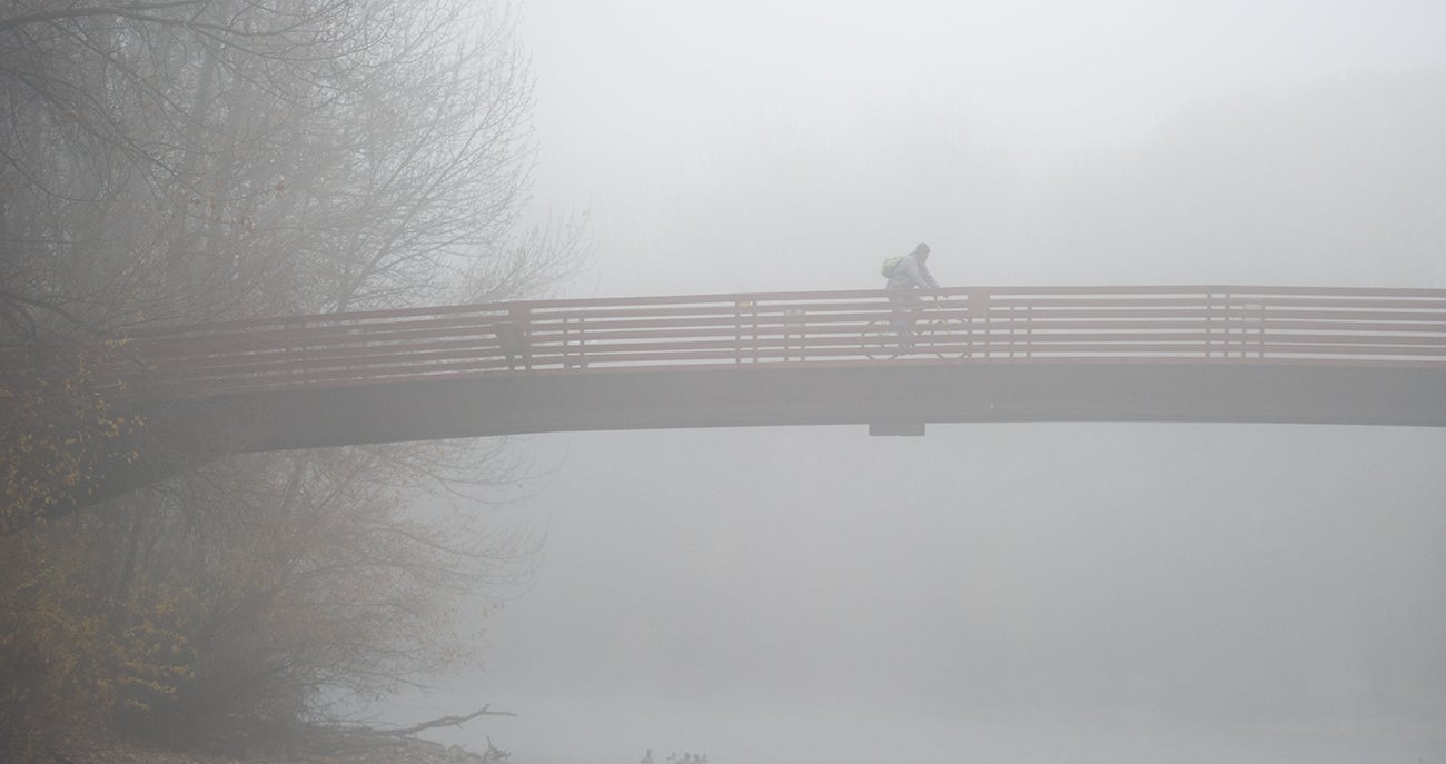 A biker crosses a bridge in thick fog.