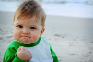 A baby grimacing and making a fist.