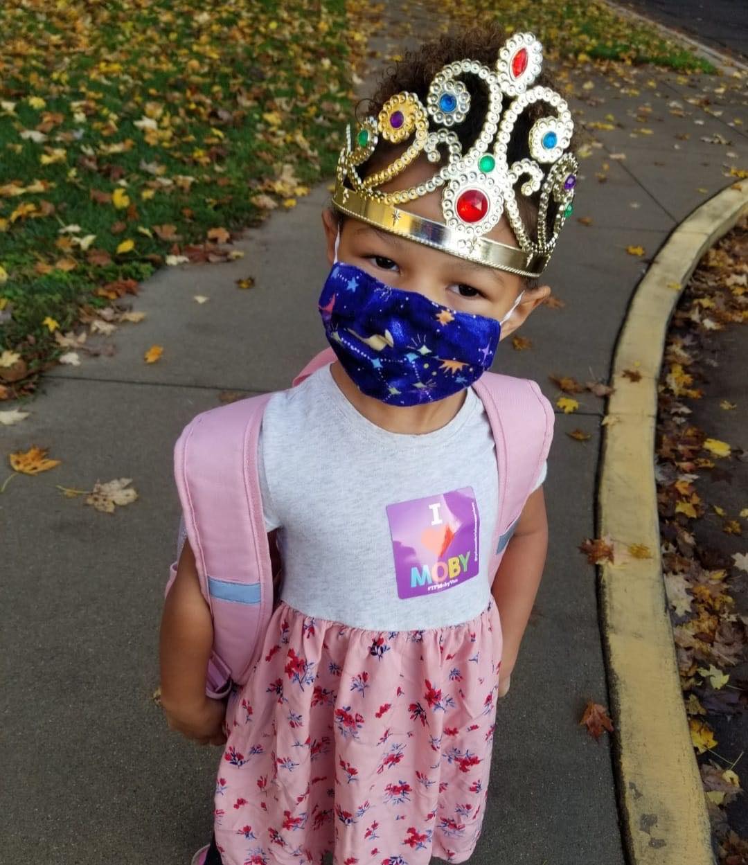 A child wearing a large tiara and a fabric face mask.