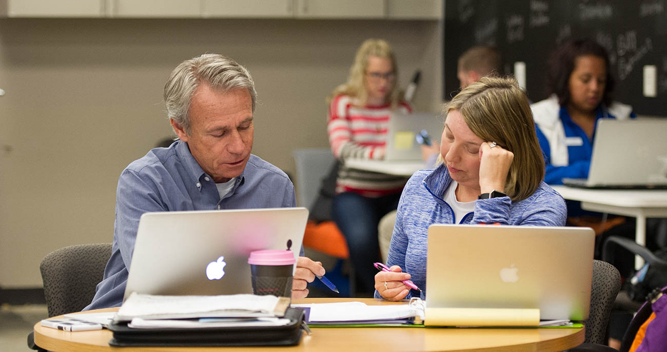 Two people working together with laptops open on table