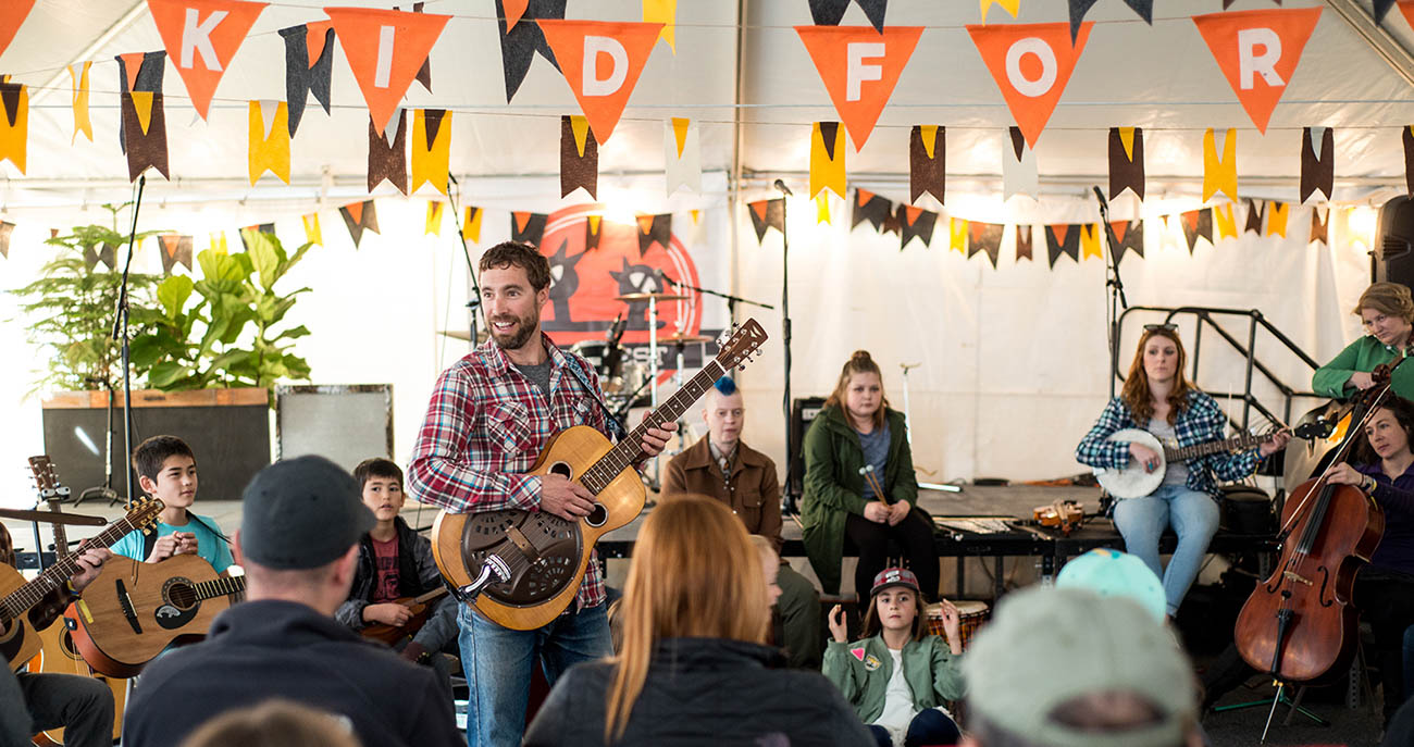 Musician with a guitar playing in front of a small indoor crowd
