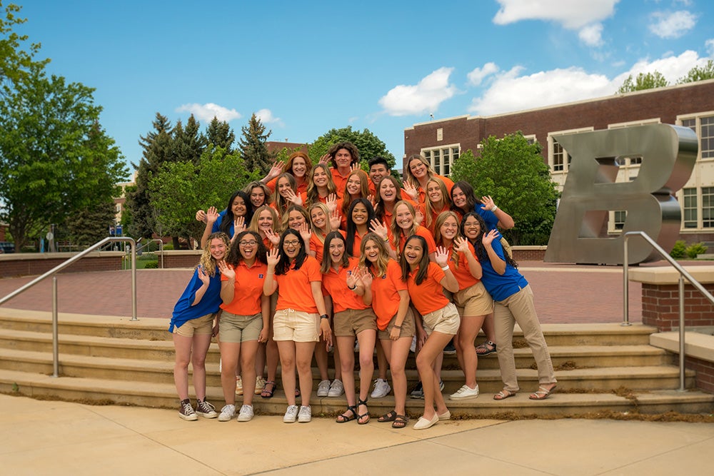 Group of students in orange polos smiling and waving