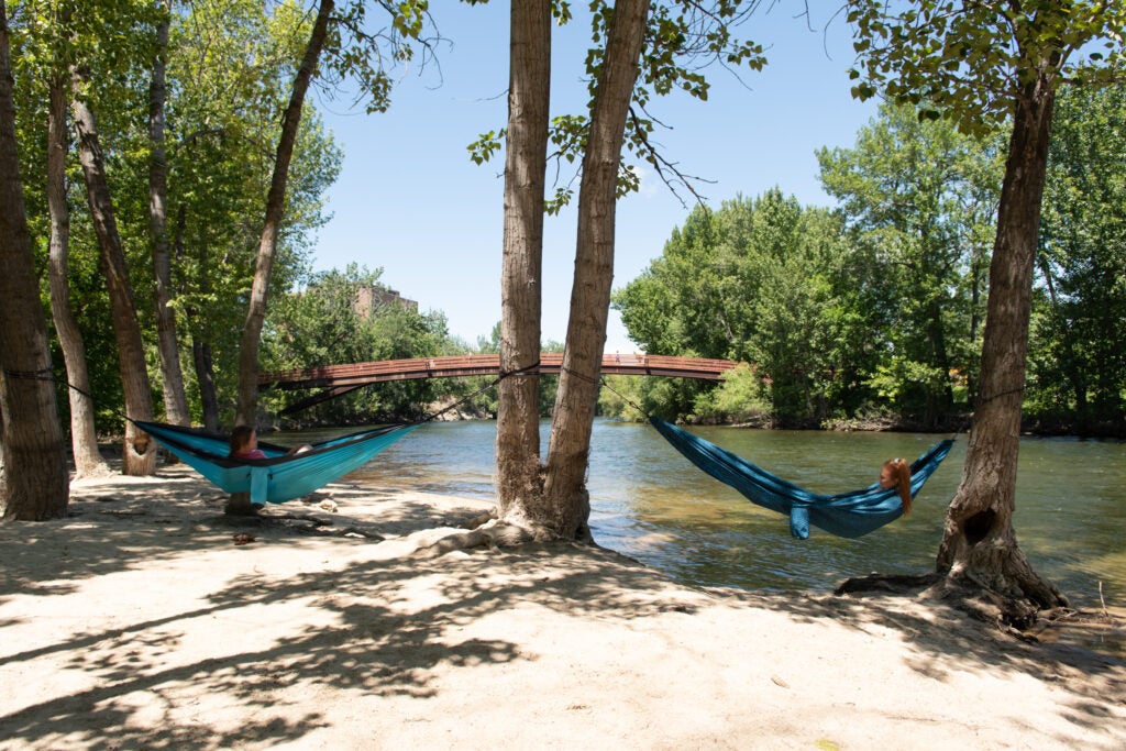 Two students lay in hammocks along the boise river.