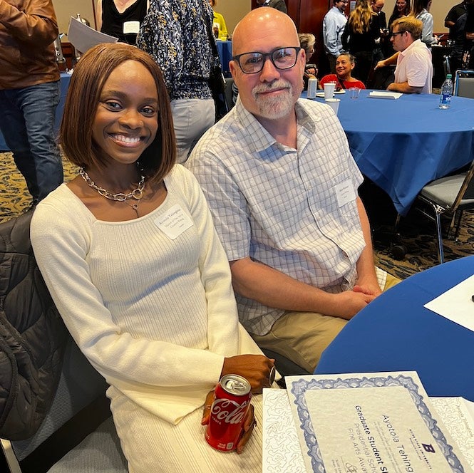 A white, bald man and a black woman sit and smile at a table with a blue covering