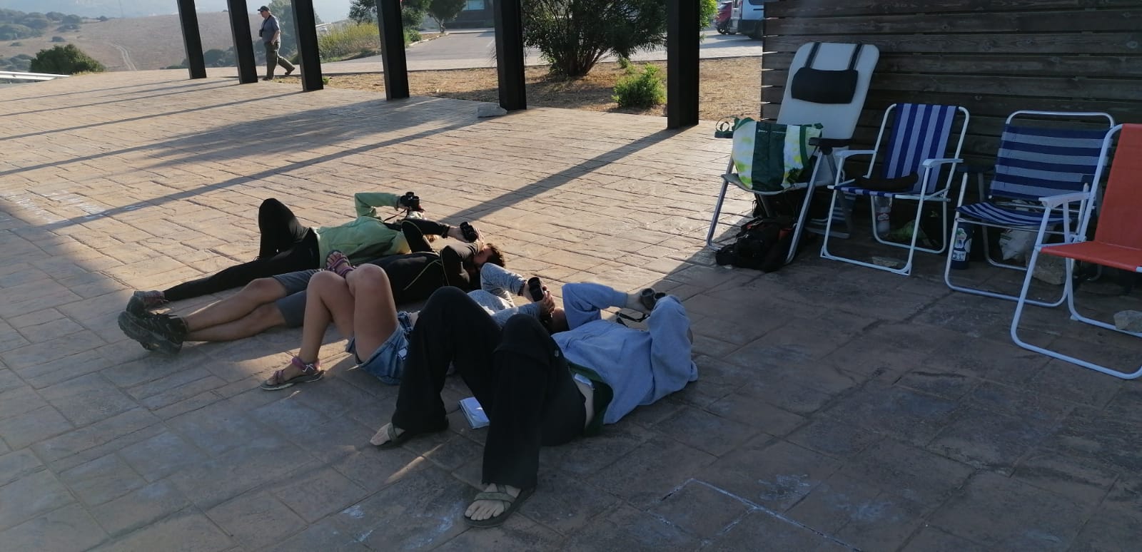 three people lay on their backs with binoculars looking up at the sky