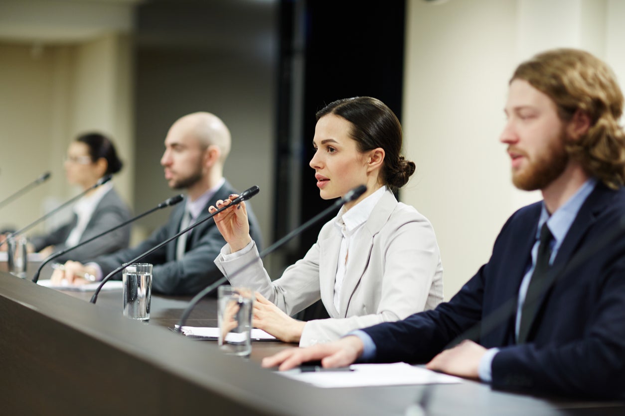 Four panelists on stage with individual microphones. 
